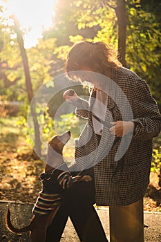 Female pet instructor in autumn clothes playing dachshund puppy in autumn park