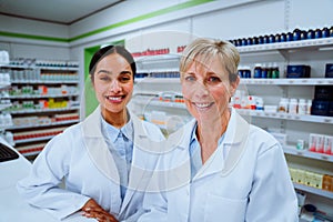 Female pharmacist smiling with mixed race doctor standing behind counter in pharmacy drugstore