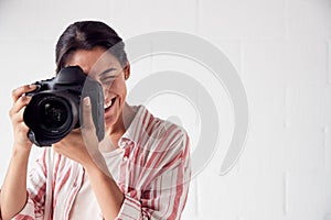 Female Photographer With Camera On Photo Shoot Against White Studio Backdrop