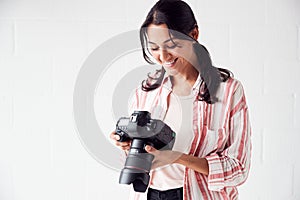 Female Photographer With Camera On Photo Shoot Against White Studio Backdrop