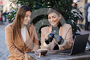 Female photographer checking pictures on camera with her client. Women sitting in cafe and drinking coffee. Work space