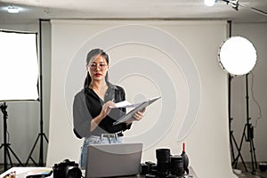 Female photographer is focusing on checking photoshoot details on a clipboard, working in her studio