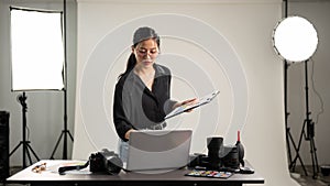 Female photographer is focusing on checking photoshoot details on a clipboard, working in her studio