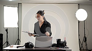 Female photographer is focusing on checking photoshoot details on a clipboard, working in her studio