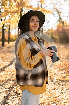 Female photographer holding professional camera in the autumn park and smiling happy portrait