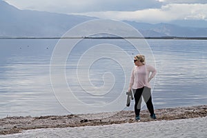 Female photographer stands on the shoreline of the Salton Sea, with her camera, staring off into the distance. Girl is wearing