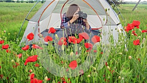 Female photographer takes picture of poppies sitting near travel tent