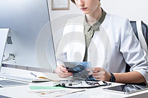 Female physician at modern medical doctor office. Woman examining x-ray at workplace in front of a desktop computer