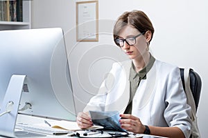 Female physician at modern medical doctor office. Woman practitioner examining x-ray at workplace in front of a desktop computer