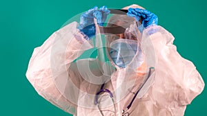 Female physician puts on a face shield wearing PPE suit uniform with stethoscope on the shoulder, wearing medical protective Mask