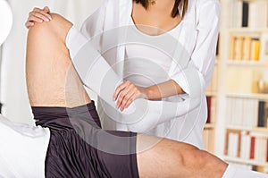 Female physio therapist hands working on male patients lower leg and ankle, bending knee, blurry clinic background