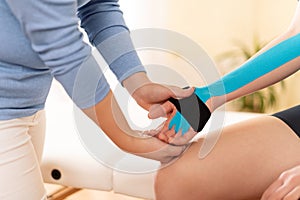 Female physiotherapist applying kinesio tape on patient`s arm. Kinesiology, physical therapy, rehabilitation concept.