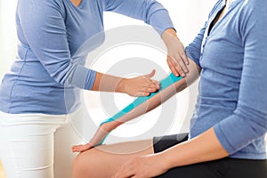 Female physiotherapist applying kinesio tape on patient`s arm. Kinesiology, physical therapy, rehabilitation concept.