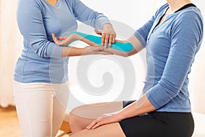 Female physiotherapist applying kinesio tape on patient`s arm. Kinesiology, physical therapy, rehabilitation concept.