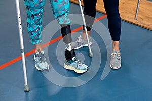 Female physiotherapist assisting disabled senior woman walk with elbow crutches in sports center