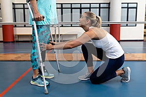 Female physiotherapist assisting disabled senior woman walk with elbow crutches in sports center