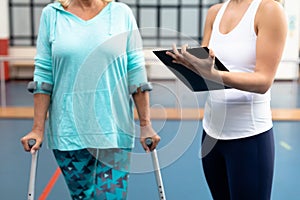 Female physiotherapist discussing with disabled senior woman on clipboard in sports center