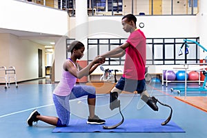 Female physiotherapist helping disabled man walk with prosthetic leg in sports center photo