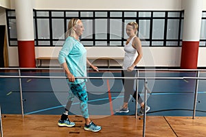 Female physiotherapist helping disabled senior woman walk with parallel bars in sports center