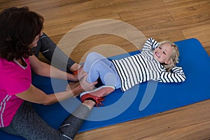 Female physiotherapist helping girl patient in performing stretching exercise on exercise mat