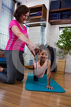 Female physiotherapist helping girl patient in performing stretching exercise on exercise mat