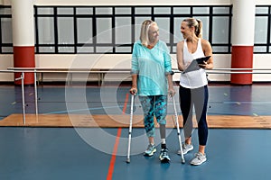 Female physiotherapist talking with disabled senior woman in sports center