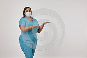 Female physiotherapist wearing a protective face mask standing while presenting and pointing with palm of hand to copy space