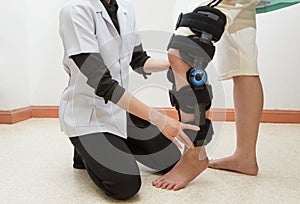 Female physiotherapy adjusting walking brace on patient`s leg in