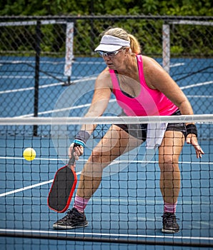 Female pickleball player digs out a low shot to dink the ball over the net