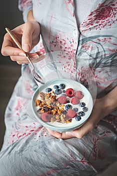 Female in pijama eating yogurt with granola and berries photo