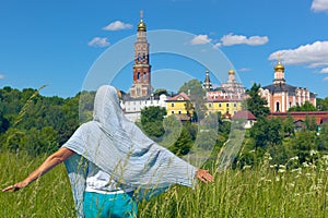 Female pilgrim in the green meadow in front of the orthodox monastery