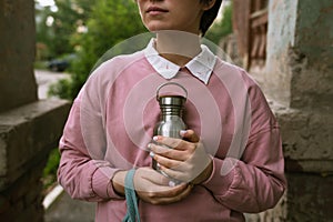 Female in pink sweatshirt holding sustainable metal eco bottle in her hands outdoors