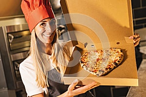 female pizza baker holding a fresh cheese pizza in a heart shape from the stone oven in a box for delivery at italian pizzeria