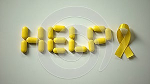 Female placing yellow ribbon, help word made of pills on table, childhood cancer