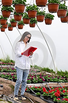 Female plant shop owner working in garden center. Woman at work in greenhouse in uniform and clipboard in her hand .