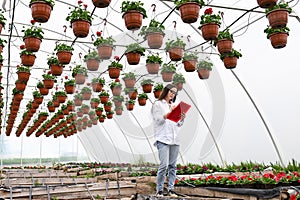 Female plant shop owner working in garden center. Woman at work in greenhouse in uniform and clipboard in her hand .