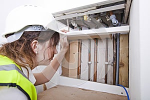 Female plumber examining pipes of central heating boiler