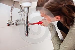 female plumber repairs or installs pipes under a sink