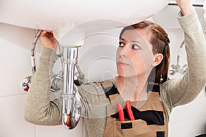 female plumber repairs or installs pipes under a sink photo