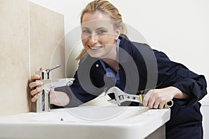 Female Plumber Working On Sink Using Wrench