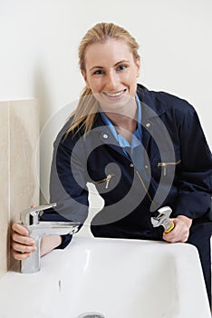 Female Plumber Working On Sink Using Wrench