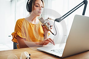 Female podcaster recording her podcast using microphone and laptop at his home broadcast studio