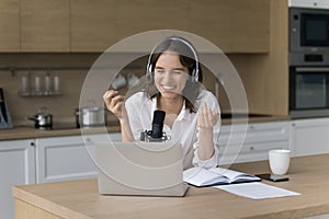 Female podcaster sits at kitchen table speaking into microphone