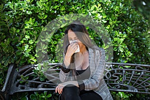 Female with pollen allergy blowing nose near bush