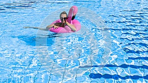 Female by pool. Happy young sexy girl in bikini swimsuit, sunglasses with pink flamingo float in blue water. Luxury lifestyle