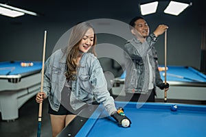 female pool player set up the billiard balls while the male player gives the chalk at the stick