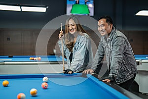 female pool player smiling while standing holding the cue stick beside the pool