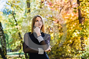 Female porteait in autumn park. Beaurtiful woman in black dress posing with yellow trees