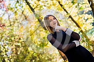 Female porteait in autumn park. Beaurtiful woman in black dress posing with yellow trees