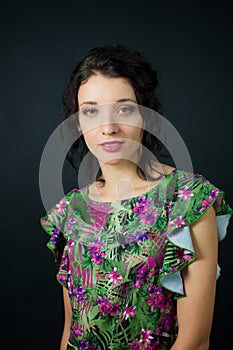 Female portrait of cute young girl in green dress with pink flowers posing in studio on black background